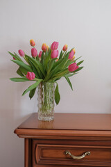 bouquet of pink and yellow tulips in vase closeup across white all on the wooden drawer. Interior detail. Hotel interior