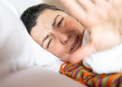 close-up portrait of woman in bed saying she doesn't want good morning pictures with hand, image with natural gesture of waking up on vacation