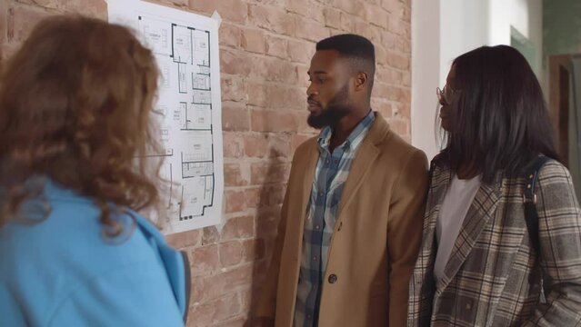 African-American couple with designer discuss blueprint of new house. Realtime