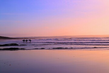 Fototapeta na wymiar Silhouette of three surfers with surfboards walking into sea and waves and sunset
