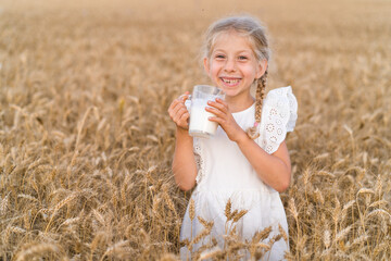 little blonde girl with pigtails in a rye field with a mug of milk, the concept of healthy eating,...