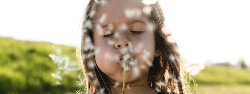 Horizontal banner or header with cute little girl with dandelion flower in countryside during a spring sunny day - Female kid having fun and blowing the seeds of dandelion outdoors