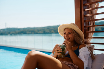 Young happy woman drinks cocktail while spending summer day by pool.
