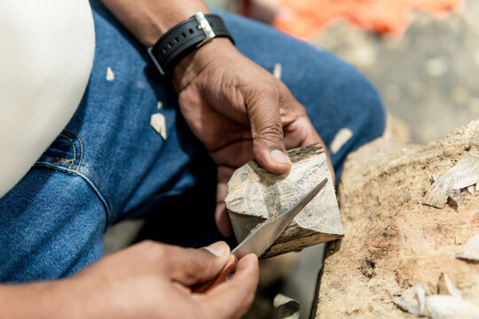 hands of senior latino man carving a jaguar in wood with knife