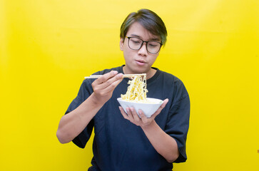 Happy attractive asian man with peek a boo hair eats noodles on bowl with chopstick