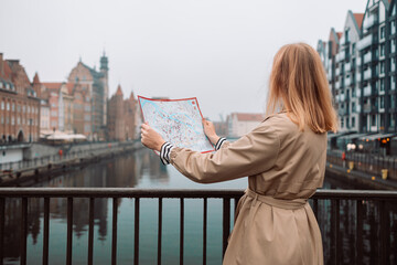 Attractive young female tourist is exploring new city. Blonde girl holding a paper map on city...