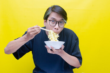 Happy attractive asian man with peek a boo hair eats noodles on bowl with chopstick