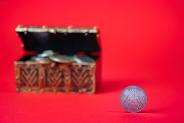 Rupee coin standing on the table, red backdrop. Blurred bank vault full of coins in the background. Saving money for future.
