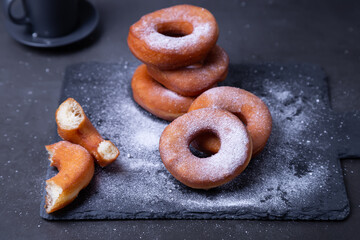 Donuts with powdered sugar and a cup of coffee. Traditional donuts in the shape of a ring fried in oil, on a black background. Junk food. Close-up.