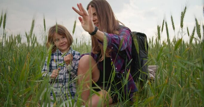 A mother and a child are touching green grass with their hands in the field. A woman tells a child about nature conservation and environmental protection. High quality 4k footage