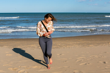 young woman walking barefoot on the beach with mat slung over her shoulder