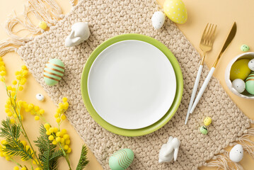 Easter celebration concept. Top view photo of empty plates cutlery colorful easter eggs ceramic bunnies cloth napkin and yellow mimosa flowers on isolated beige background