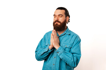 Humble bearded man with eyes closed is holding hands together and praying.