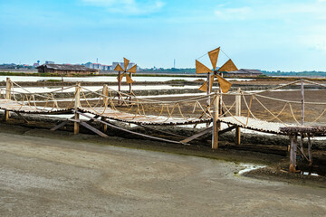 Fototapeta na wymiar Wooden turbine at salt pan using for press seawater up to field with blue sky background in summer time of Thailand,South East Asia. Beautiful landscape of salt fields.Traditional salt farming culture