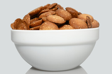 Small sesame biscuits in a white cup. On a gray background.