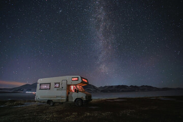 motor home under the starry sky against the backdrop of the mountains in winter