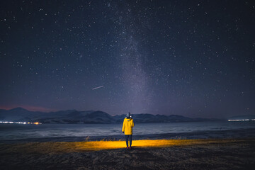 man stands under the starry sky and the milky way against the backdrop of mountains