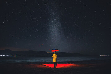 man with an umbrella stands under the starry sky and mountains in the background