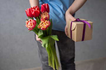 The boy hides a bouquet of flowers and a box with a gift for his mother behind his back