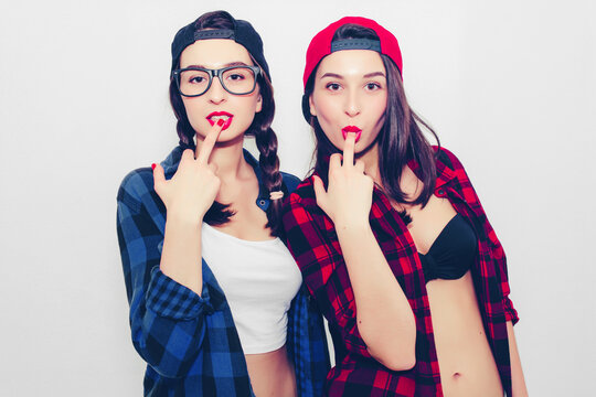 Colorful comic emotional hipster twin girls in baseball cap, topless, smile, cover mouth with hands, surprised and show tongue. Isolated on a light background.