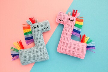 Crochet amigurumi handmade stuffed soft colored unicorn toys with rainbow mane on pink and blue background. Handwork, hobby. Craft diy newborn pregnancy concept. Knitted doll for little baby. Close-up
