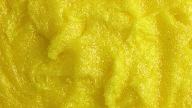 Top view of bright yellow lemon exfoliating sugar body scrub texture circle rotation close up