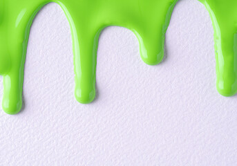 Light green liquid drops of paint color flow down on white canvas. Abstract art. Paint dripping on the white wall with copy space.