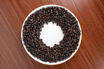 Coffee beans are placed on a plate with a wooden board in the background.  There is space for text or something.