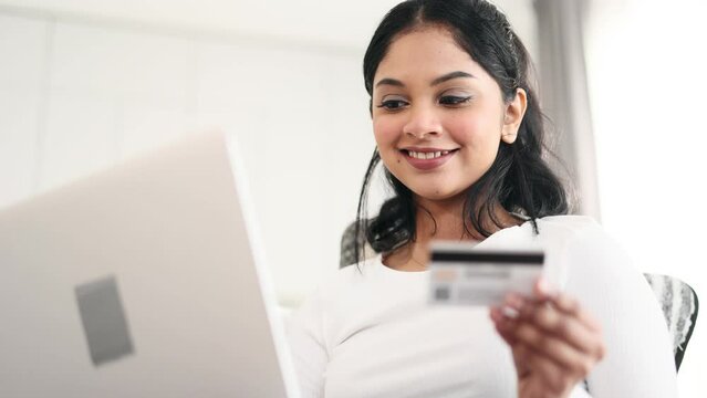 Portrait of young indian woman paying with credit card on laptop computer at home Happy customer doing payments online shopping in internet store and receiving cashback Easy pay concept