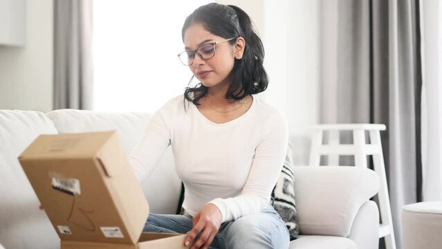 Portrait of indian young woman received parcel dissatisfied with shopping in online internet store sitting on sofa at home Upset customer disappointed with purchase order while opening carton box