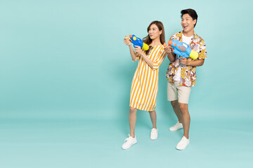 Young Asian couple in summer outfits holding water guns plastic for Songkran festival in Thailand isolated on green background - 578415896