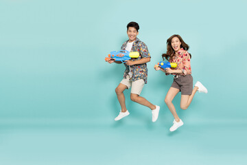 Fototapeta na wymiar Young Asian couple in summer outfits jumping and holding water guns plastic for Songkran festival in Thailand isolated on green background