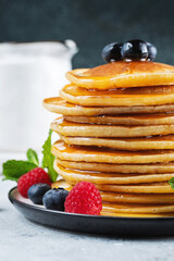 Delicious pancakes, with fresh blueberries, raspberry and maple syrup or honey on a dark background