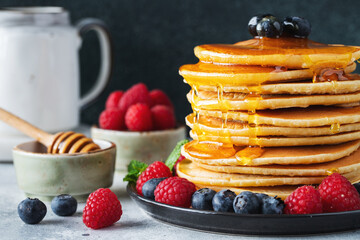 Delicious pancakes, with fresh blueberries, raspberry and maple syrup or honey on a dark background
