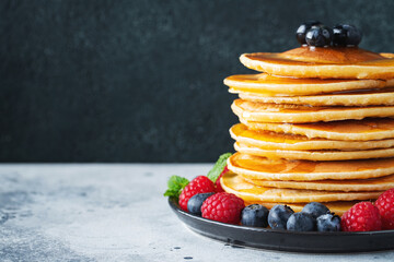 Delicious pancakes, with fresh blueberries, raspberry and maple syrup or honey on a dark background
