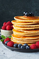 Delicious pancakes, with fresh blueberries, raspberry and maple syrup or honey on a dark background