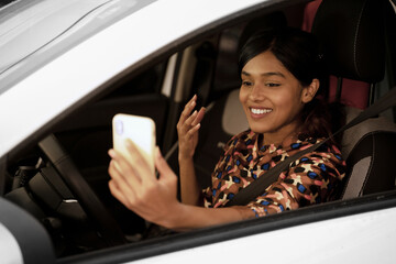 Busy smiling Indian woman using mobile phone communication online, driving car. Distracted driving...