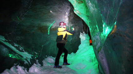 A girl with a neon lamp stands in an ice cave. The white light is highlighted with a bright green...