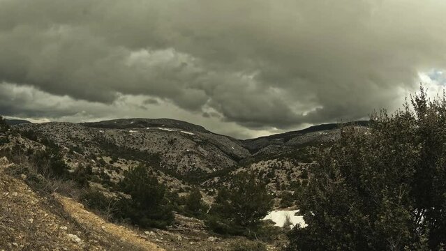Time lapse video shows dark clouds passing by over a mountain's peak with spots covered of old snow.