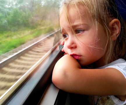 Little girl looks through the window. She travels on a train