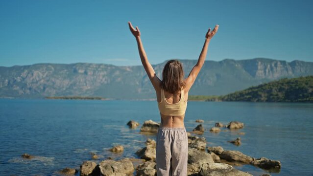 Back view woman practices yoga with hands up pose at nature with beutiful mountains view. Body and mental welness