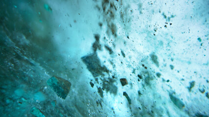 Turquoise pure color of ice inside the ice cave. Stones and icicles are visible in places. Light grains of snow on the ice walls. Frozen air bubbles in an ice wall. An ancient glacier. Color gradient