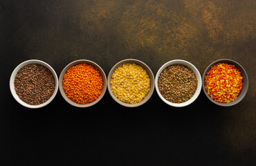 Multicolored lentils in bowls on a brown background, yellow and brown, green and orange lentils, healthy legumes, top view, copy space