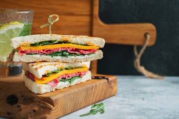 Two homemade sandwiches with sausage, cheese and arugula on a light concrete background
