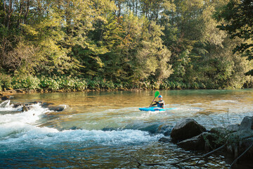 Young teenager cruising down whitewater rapids in a blue kayak, beautiful river nature on a sunny...