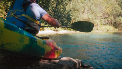 Man in kayak equipment descending into a river, coming down into the water over a wooden ramp, rear...
