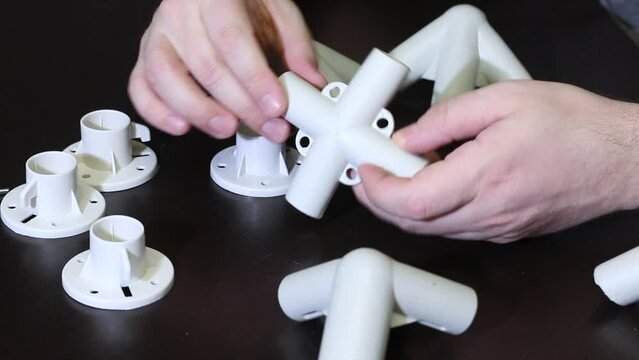 A man demonstrates a set of parts for a garden awning. Examines adapters and supports. Close-up.