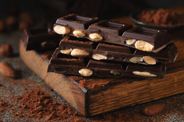 Dark and milk chocolate with nuts on a dark background sprinkled with cocoa powder.