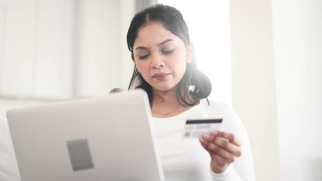 Portrait of young indian woman paying with credit card on laptop computer at home Happy customer doing payments online shopping in internet store and receiving cashback Easy pay concept