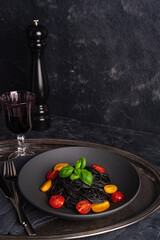 Black spaghetti with tomatoes and basil  in the black plate on a dark background, Glass of wine.  Top view..